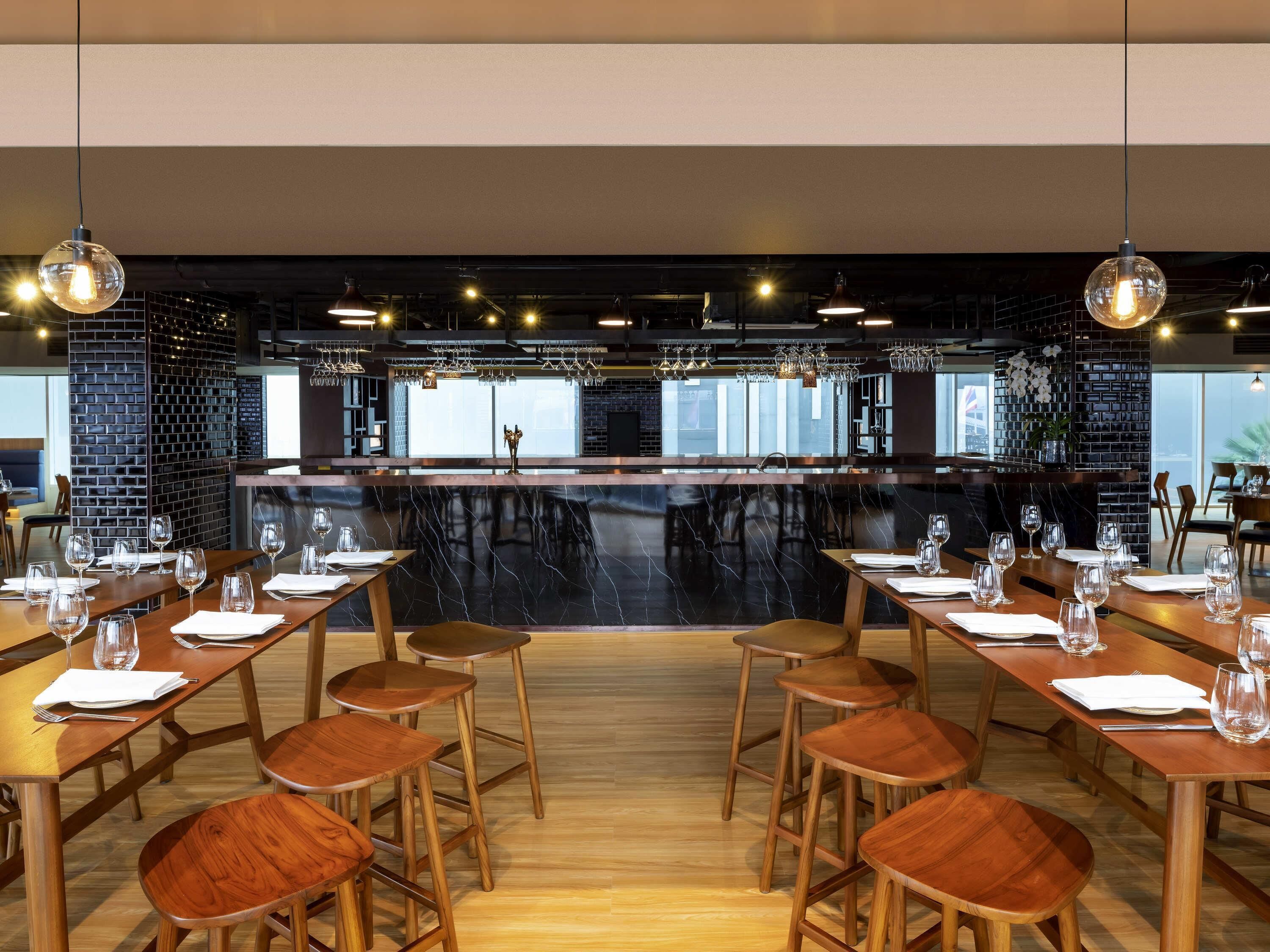 A restaurant with a central bar, wooden tables, and hanging light fixtures.