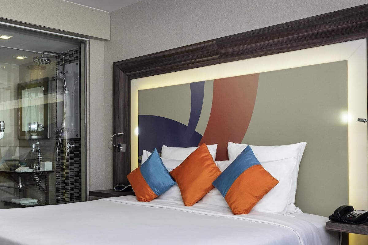 Une chambre d’hôtel équipée d’un lit, d’un téléphone sur la table de chevet et d’une douche séparée par des parois en verre.