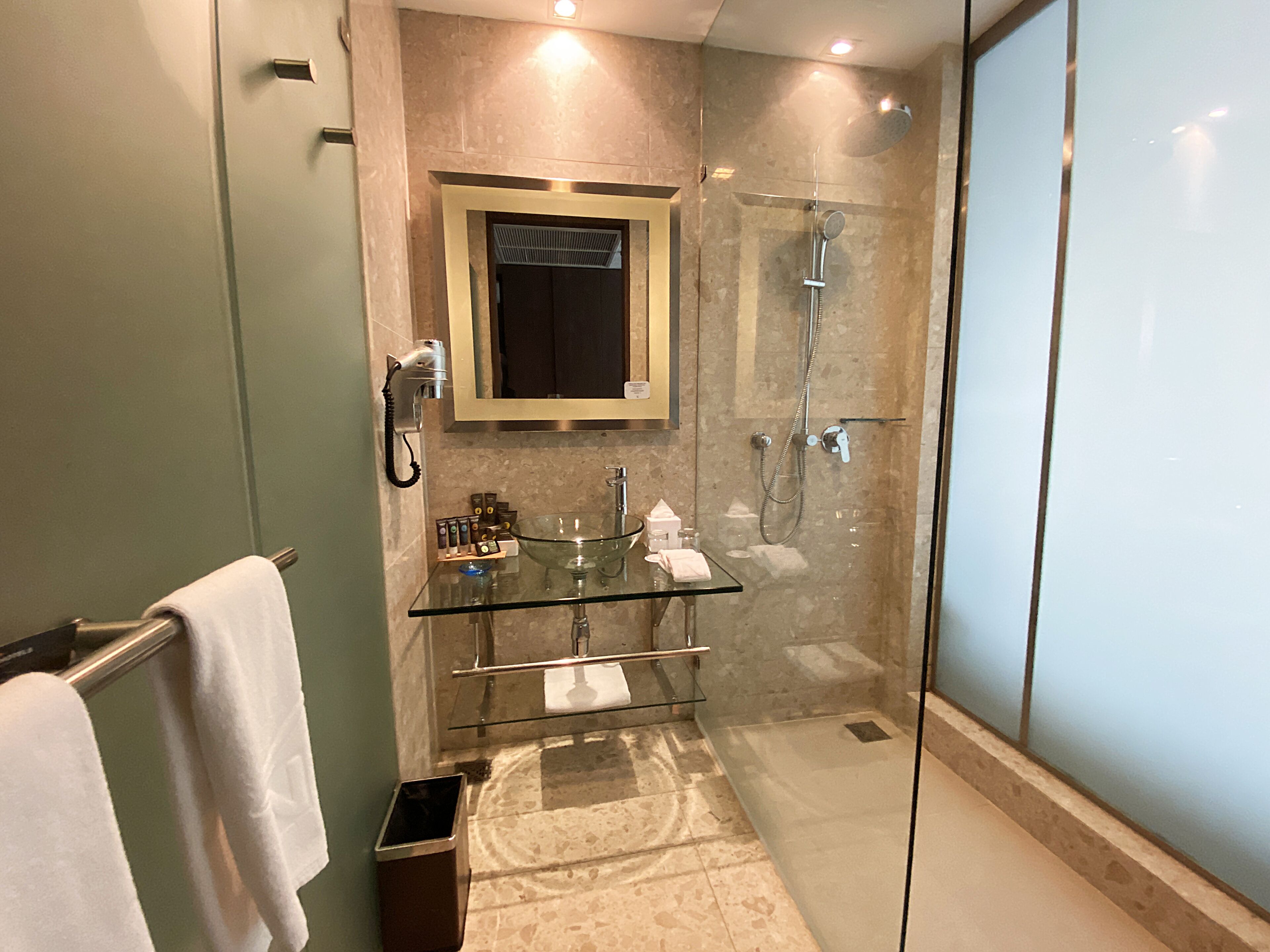 Een moderne badkamer met een douche met glazen wanden, een glazen wasbak en een handdoekhouder.