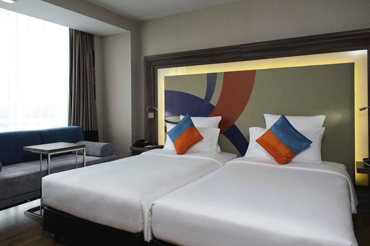 A hotel room with two beds, a sofa, a desk, and a large abstract painting on the wall.
