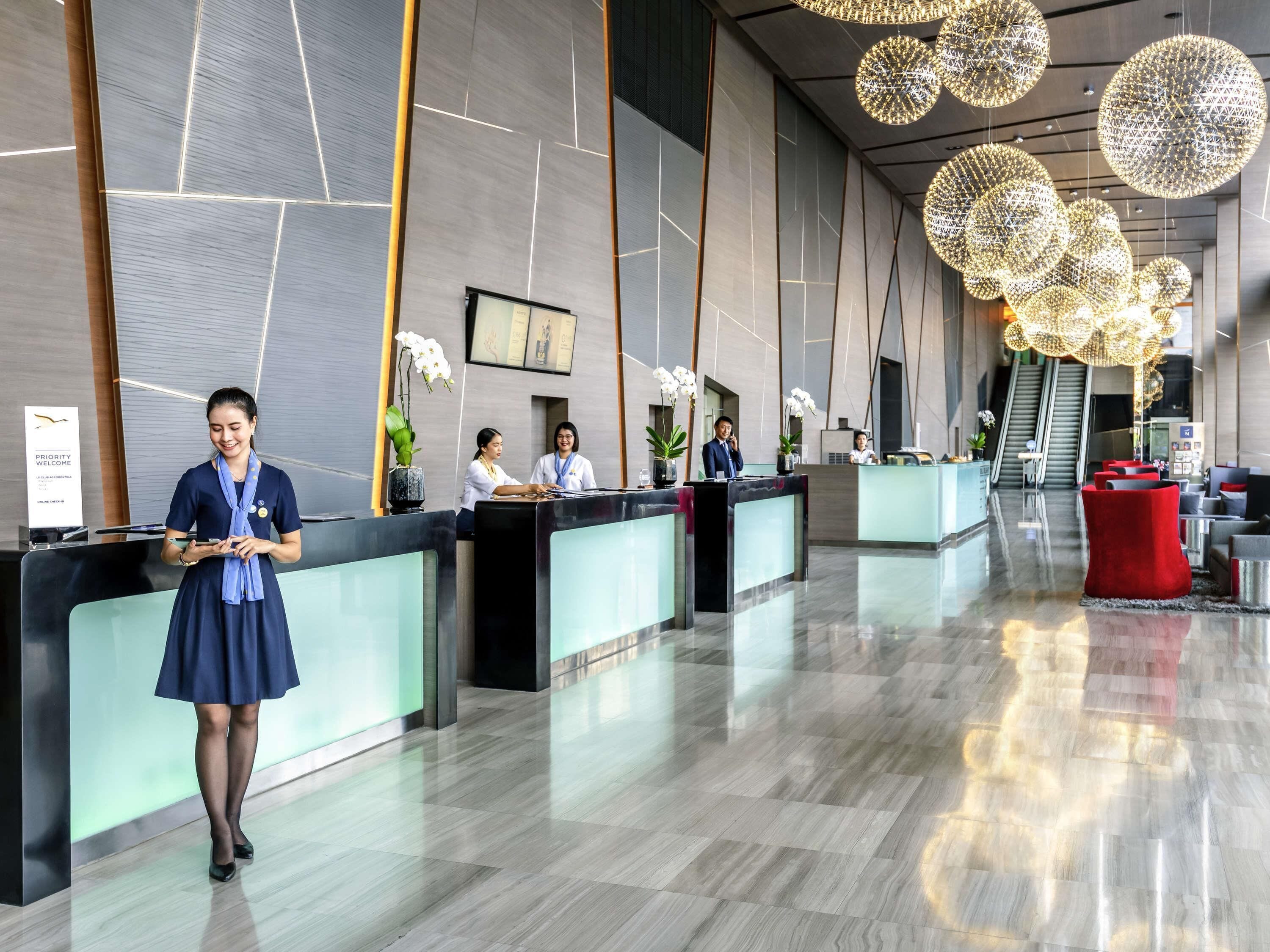 A modern hotel reception area with a glass partition, a receptionist, and reception staff.