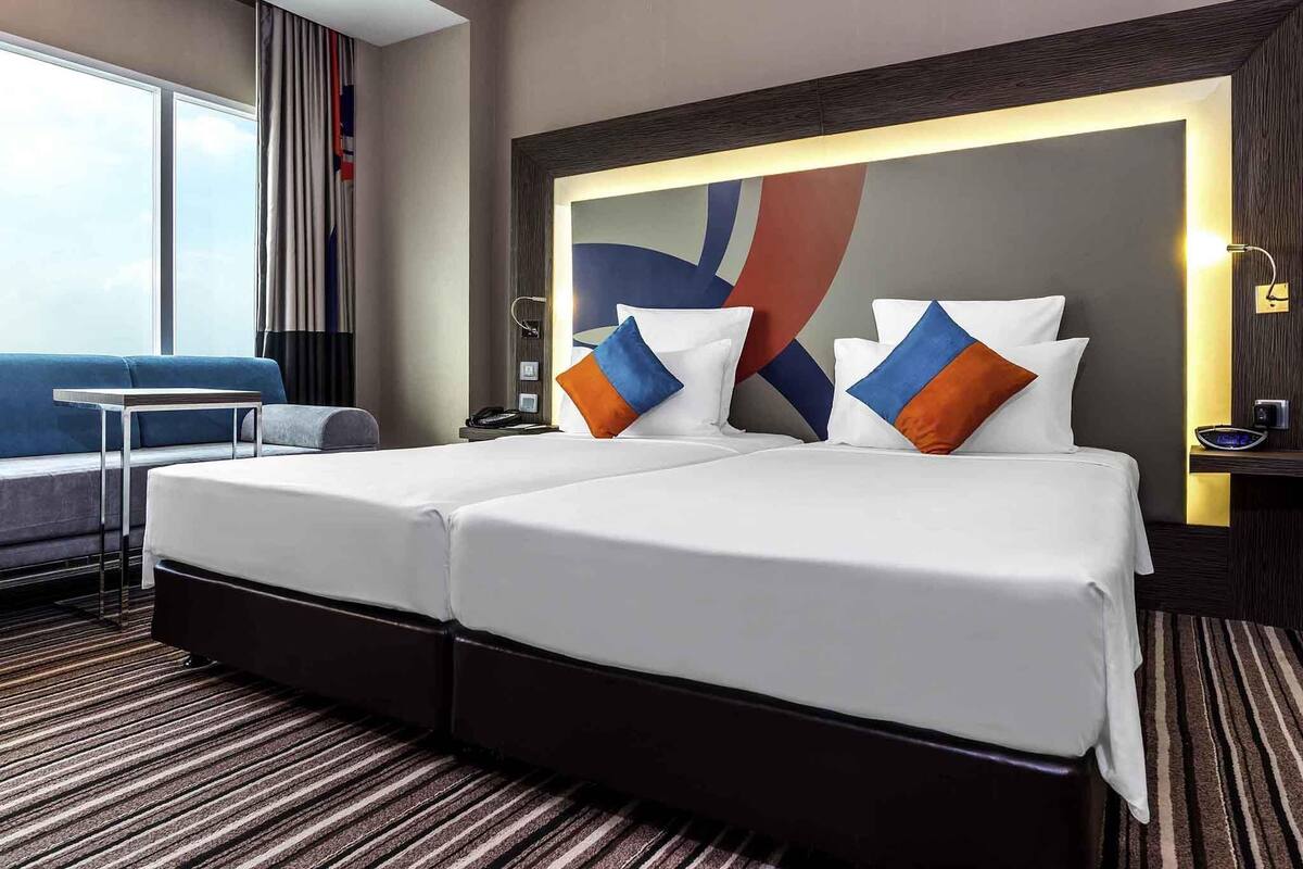 A hotel room with a large bed, a sofa, a desk, and a view of the sky.
