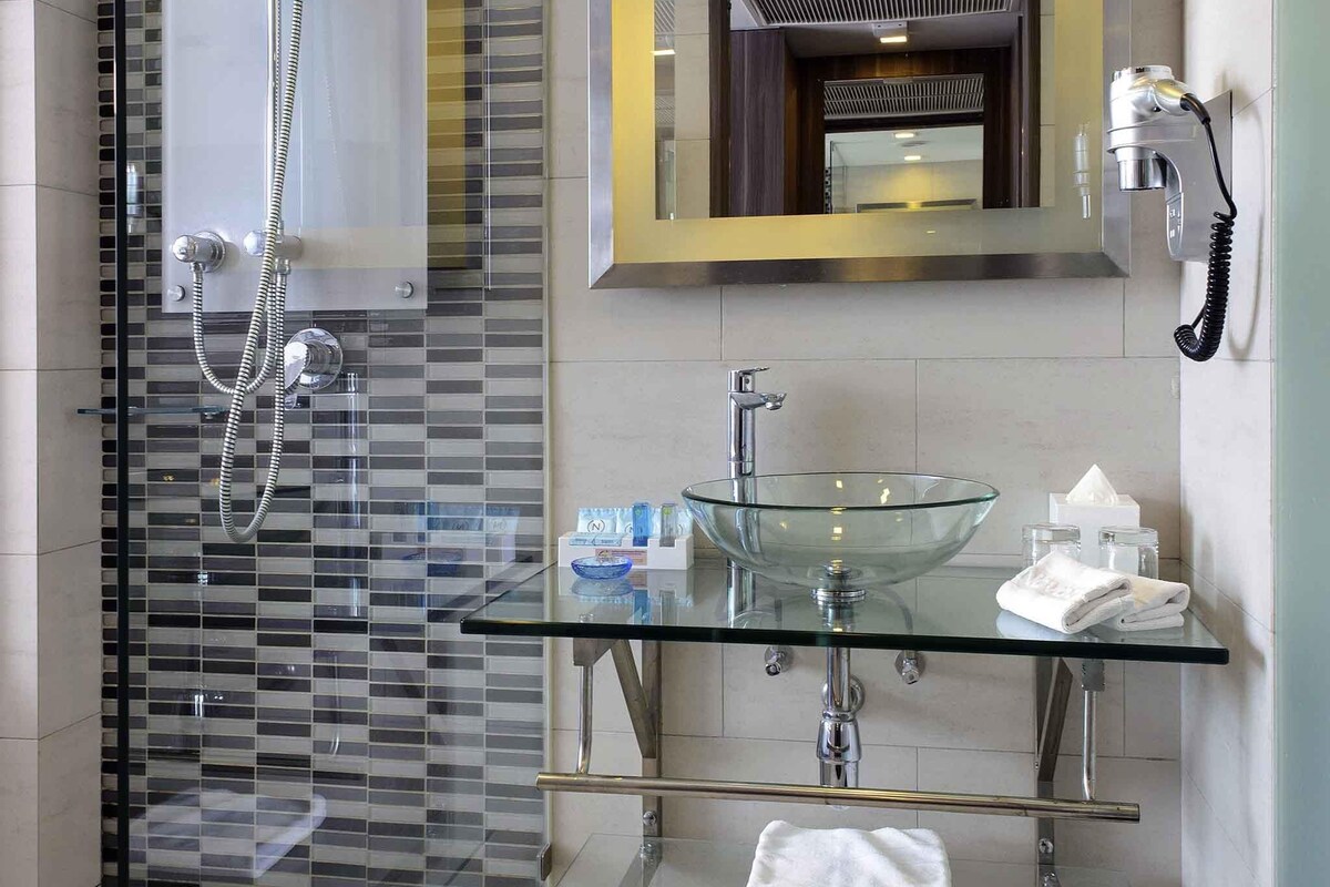 A modern bathroom with a glass-enclosed shower, a glass sink, and a mirror with a telephone.