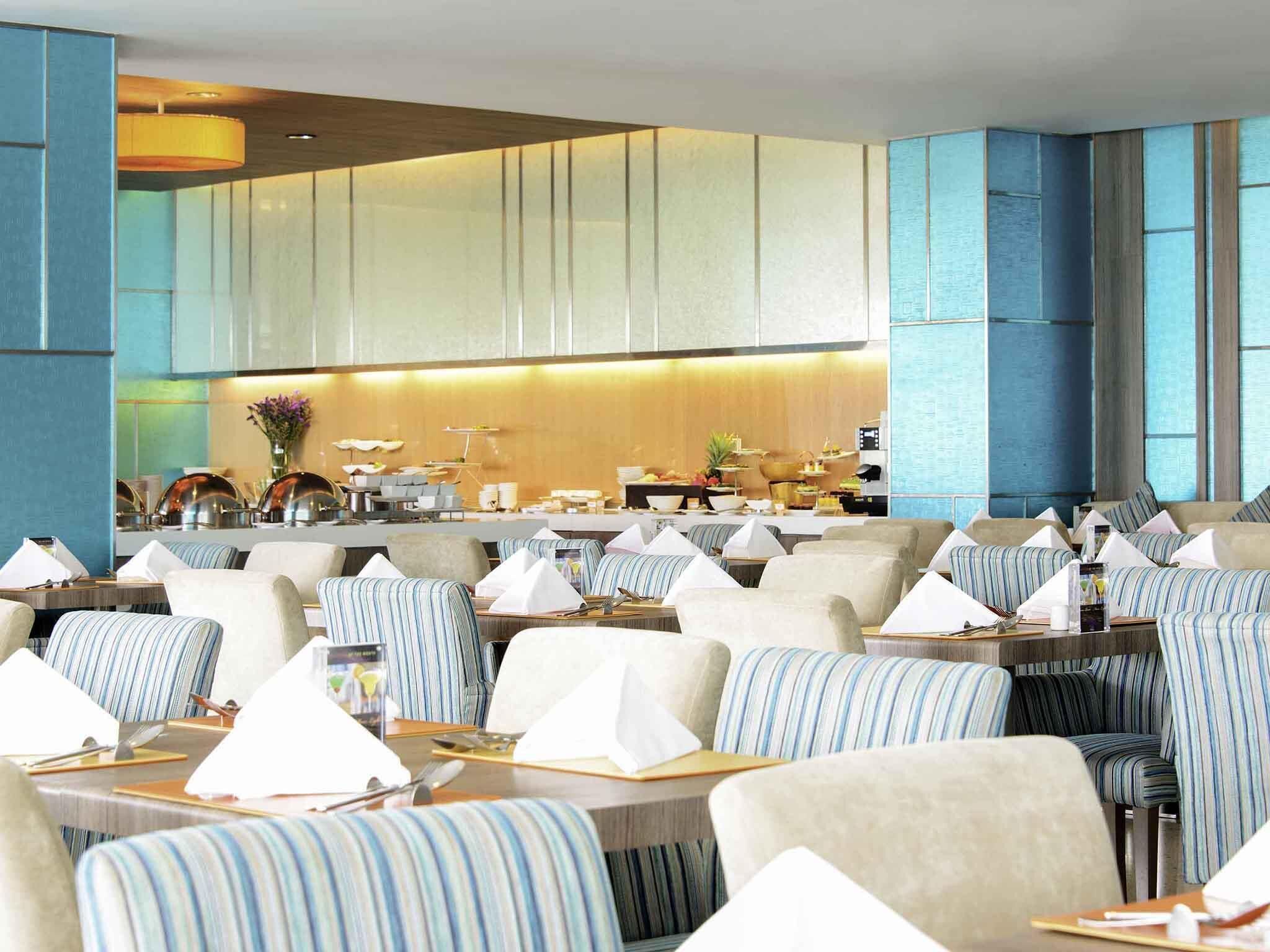 Een restaurant met gestreept beklede stoelen, tafels met witte servetten en een keuken op de achtergrond.