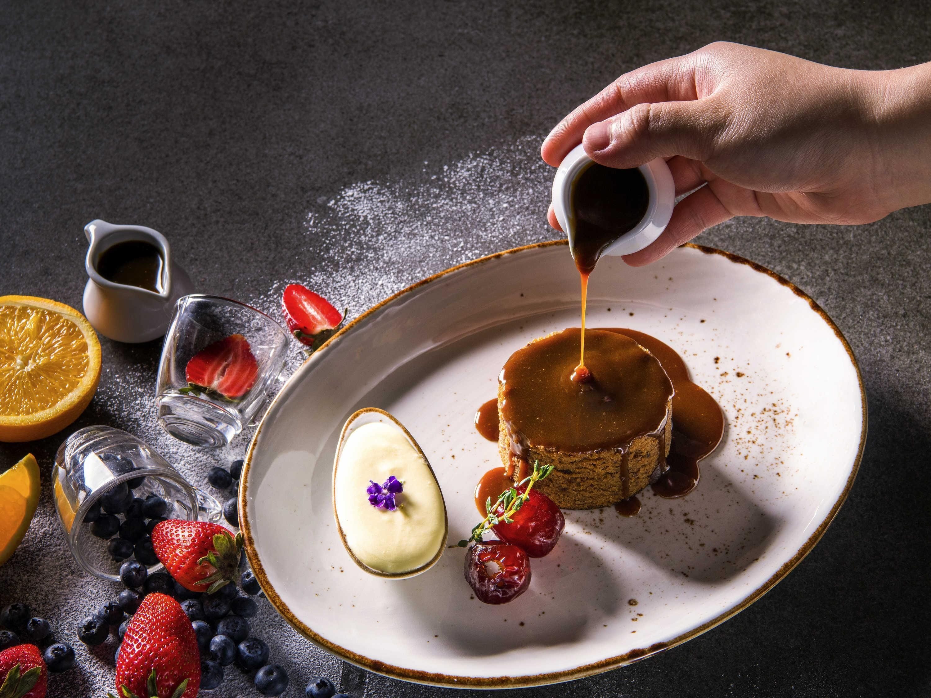 A dessert plate with caramel sauce being poured, surrounded by strawberries and blueberries.