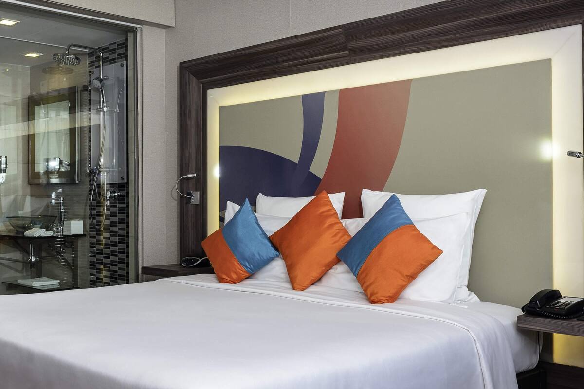 A hotel room with a bed, a glass shower enclosure, and a bedside phone.