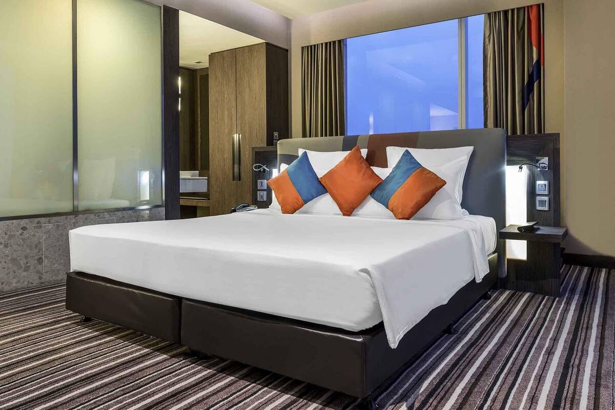 A hotel room with a large bed, a nightstand, a mirror, and a window with curtains.