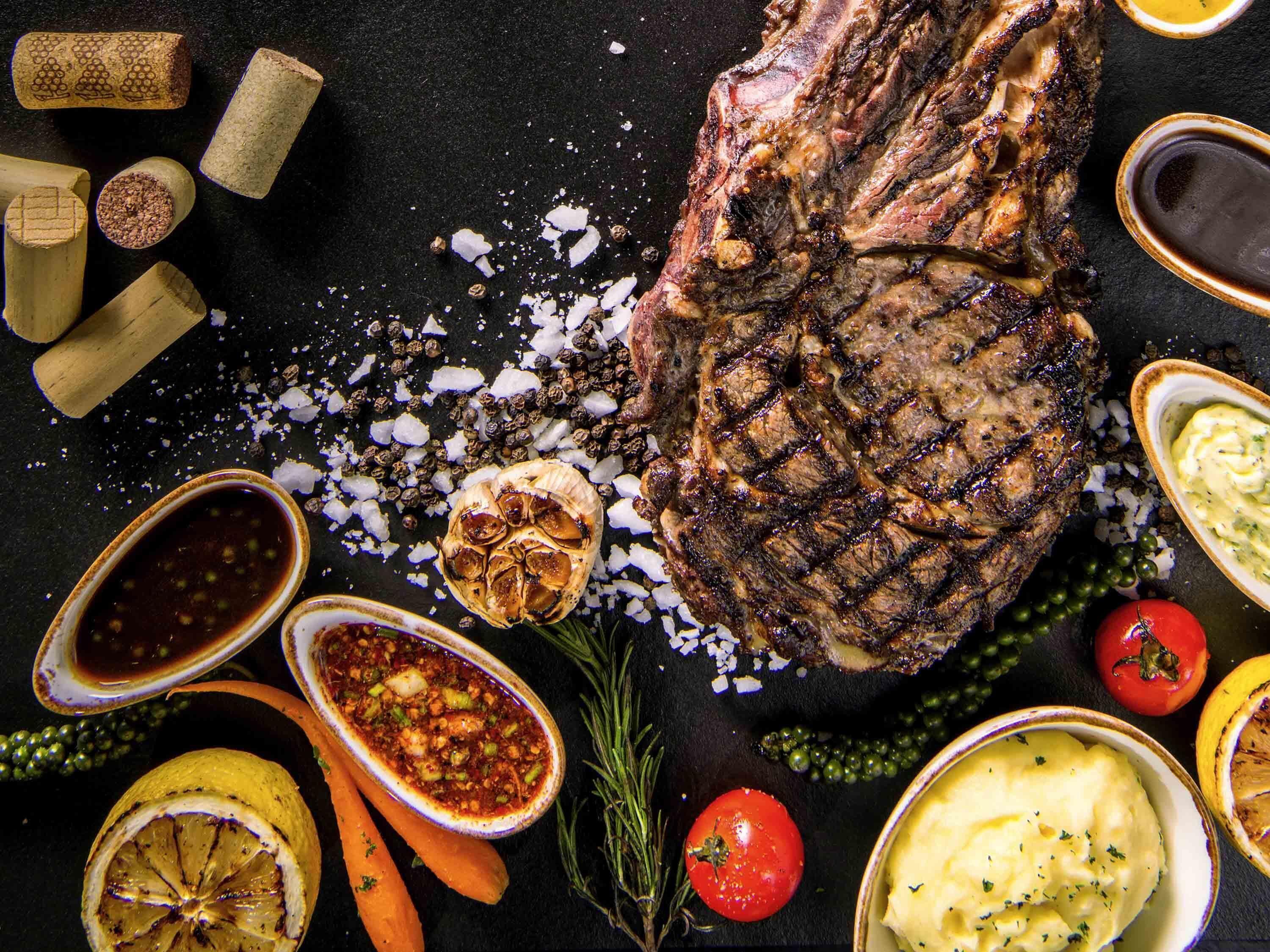 A steak with various condiments and vegetables on a dark background.