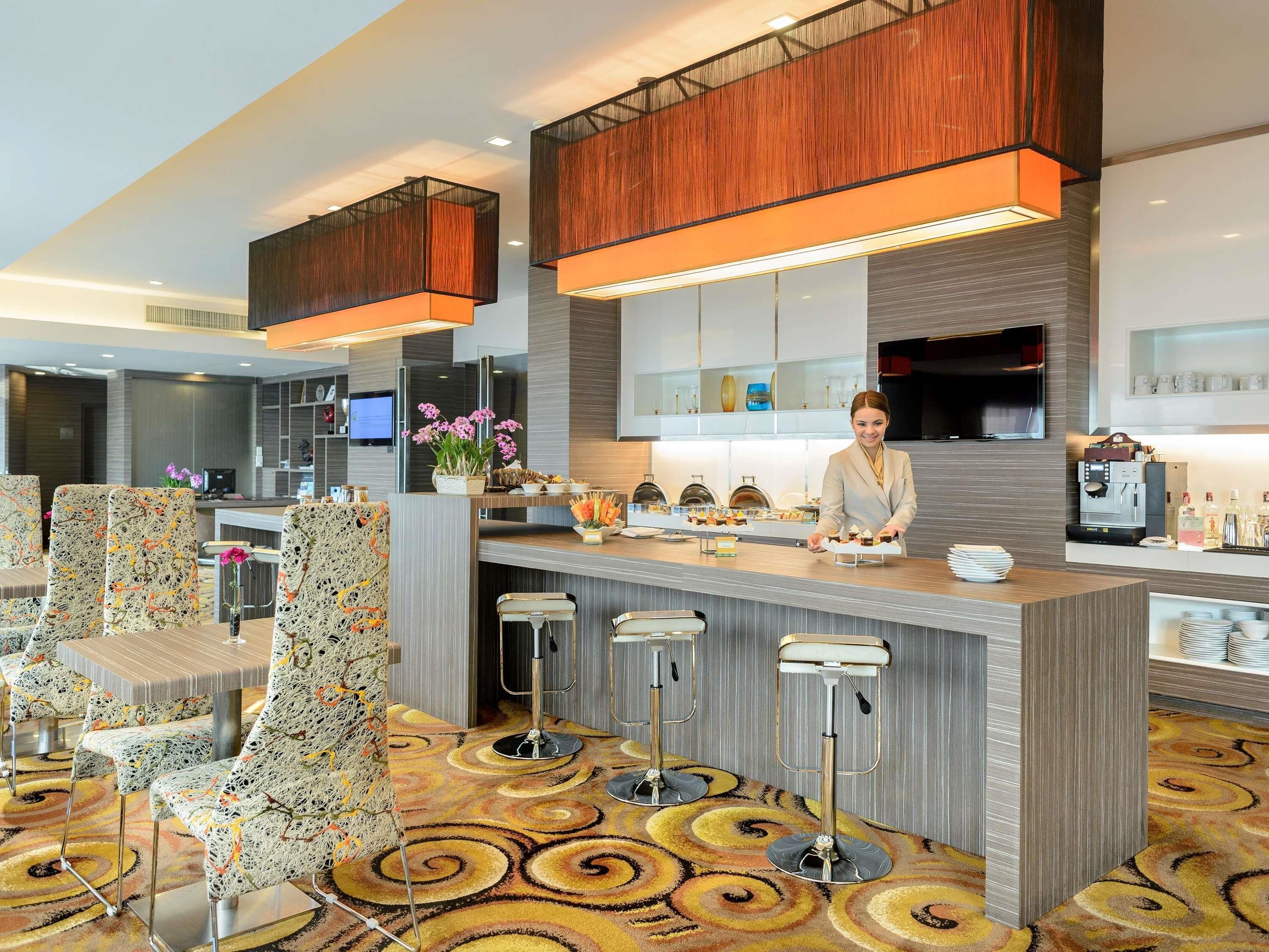 A modern hotel lobby with a central bar area, seating arrangements, and a decorative carpet.