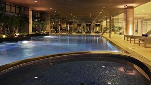 An indoor swimming pool with exercise equipment, surrounded by glass walls and indoor plants. - Novotel Bangkok IMPACT (Pak Kret)