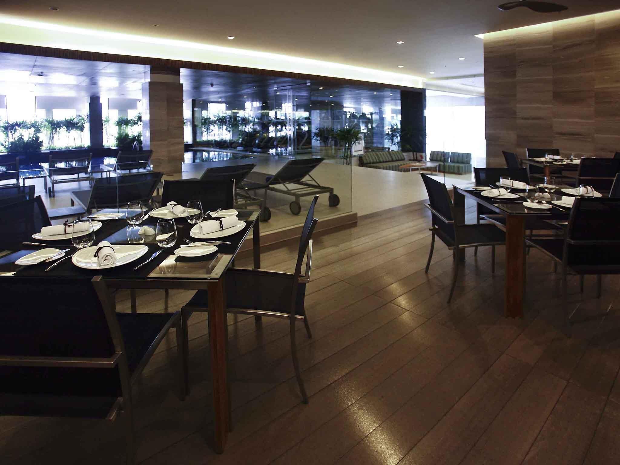 A modern dining area with tables set for service, a view of the airport terminal, and a seating area with a sofa and coffee table.
