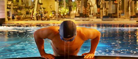 A man in a swimming cap at the edge of a pool with gym equipment in the background.