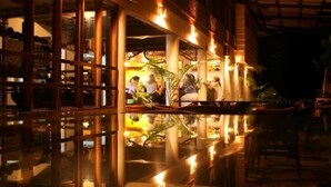 An indoor area with a reflective floor, wooden columns, and a group of people gathered around a table. - Selva Verde Lodge (Puerto Viejo)