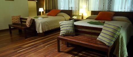 Habitación de hotel con dos camas, suelo de madera y un banco.