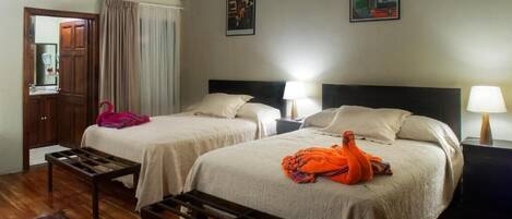 A hotel room with two beds, a wooden bench, a ceiling fan, and a window with curtains.