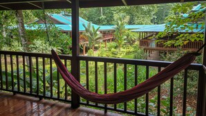 A hammock on a wooden deck with a view of a lush garden and buildings with blue roofs. - Selva Verde Lodge (Puerto Viejo)