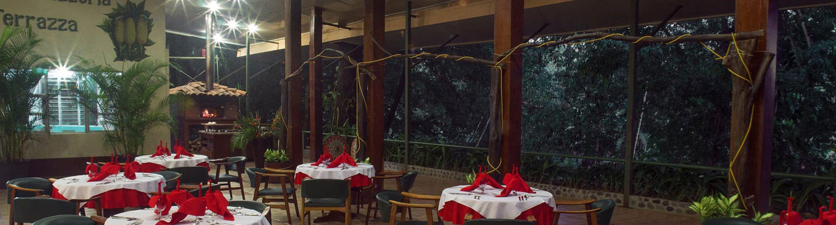 A restaurant with tables set for dining, surrounded by plants and a view of trees.
