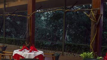 A restaurant with tables set for dining, surrounded by plants and a view of trees.