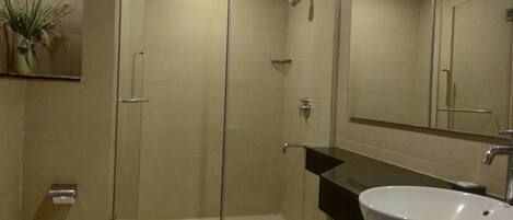 Un baño moderno con ducha de vidrio, lavamanos blanco y espejo sobre el lavamanos.