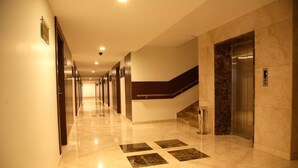 A hotel corridor with a marble floor, a staircase, and an elevator.