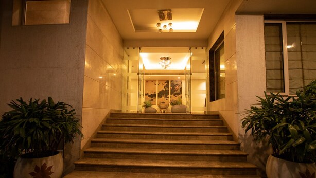 A staircase leading to a lobby with glass doors, potted plants, and a chandelier.