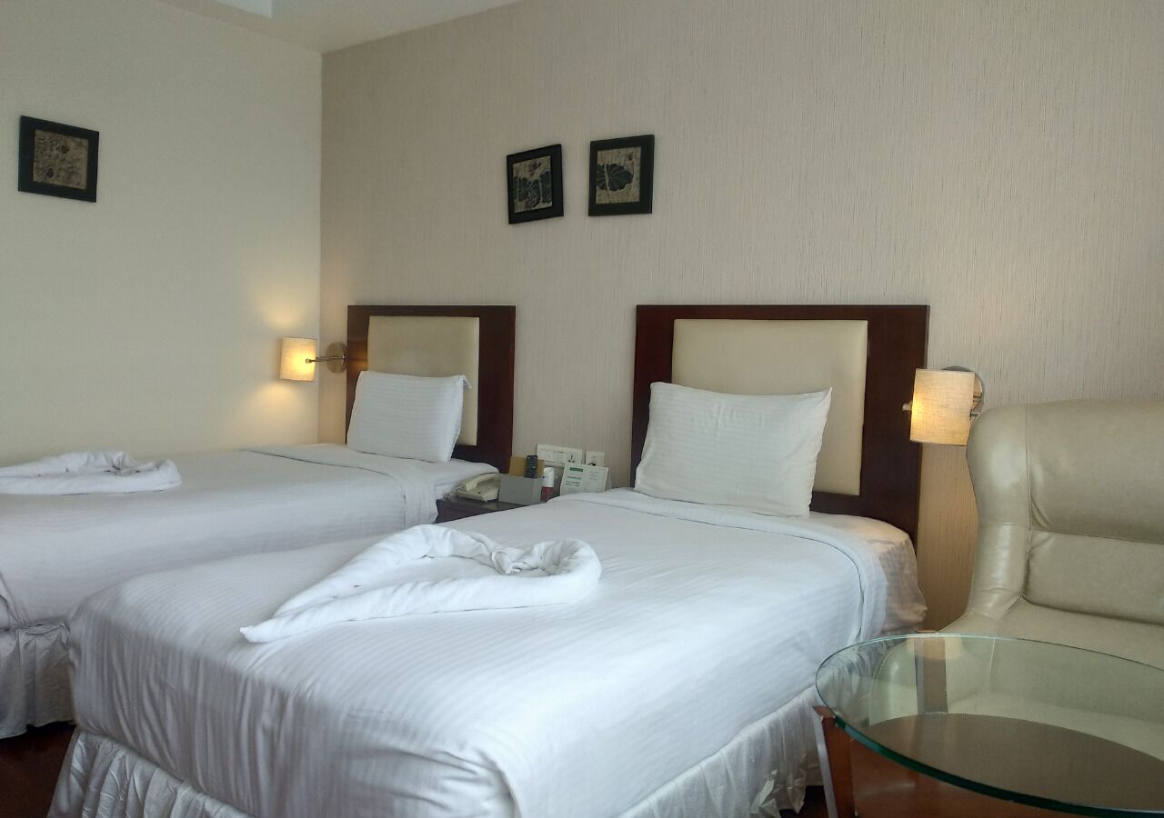 Habitación de hotel con dos camas, una mesita de vidrio y una silla.