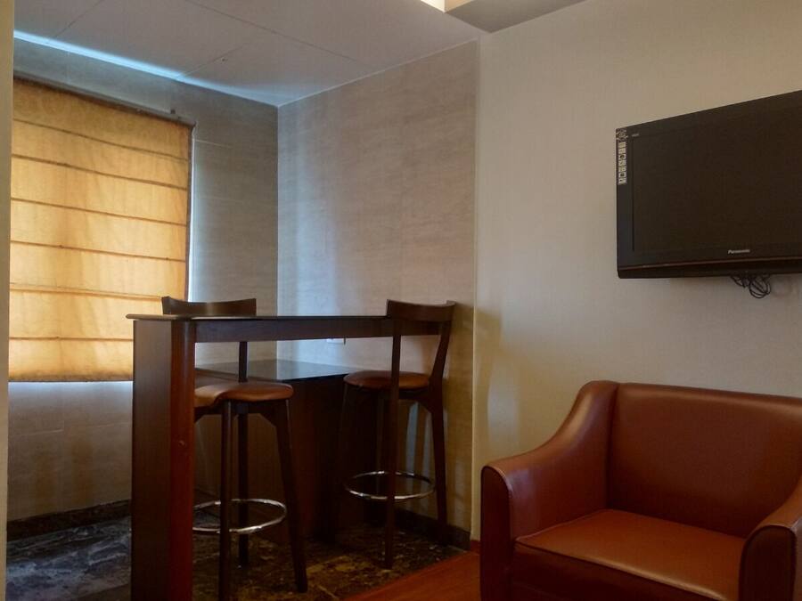 A room with a wooden table and chairs, a leather sofa, and a mounted television.