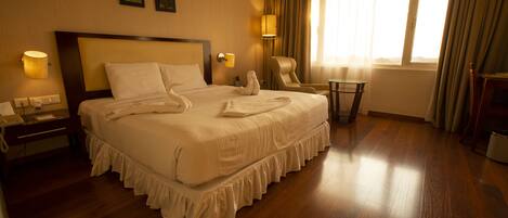 A hotel room with a large bed, a chair, a small table, and a lamp.