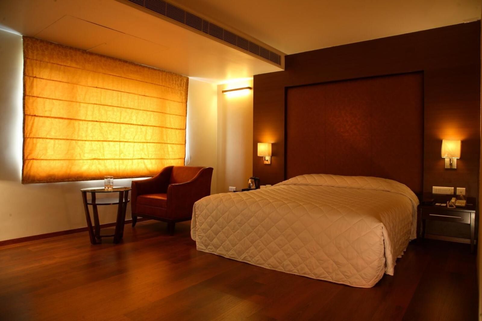 A hotel room with a large bed, a chair, a small table, and a window with blinds.