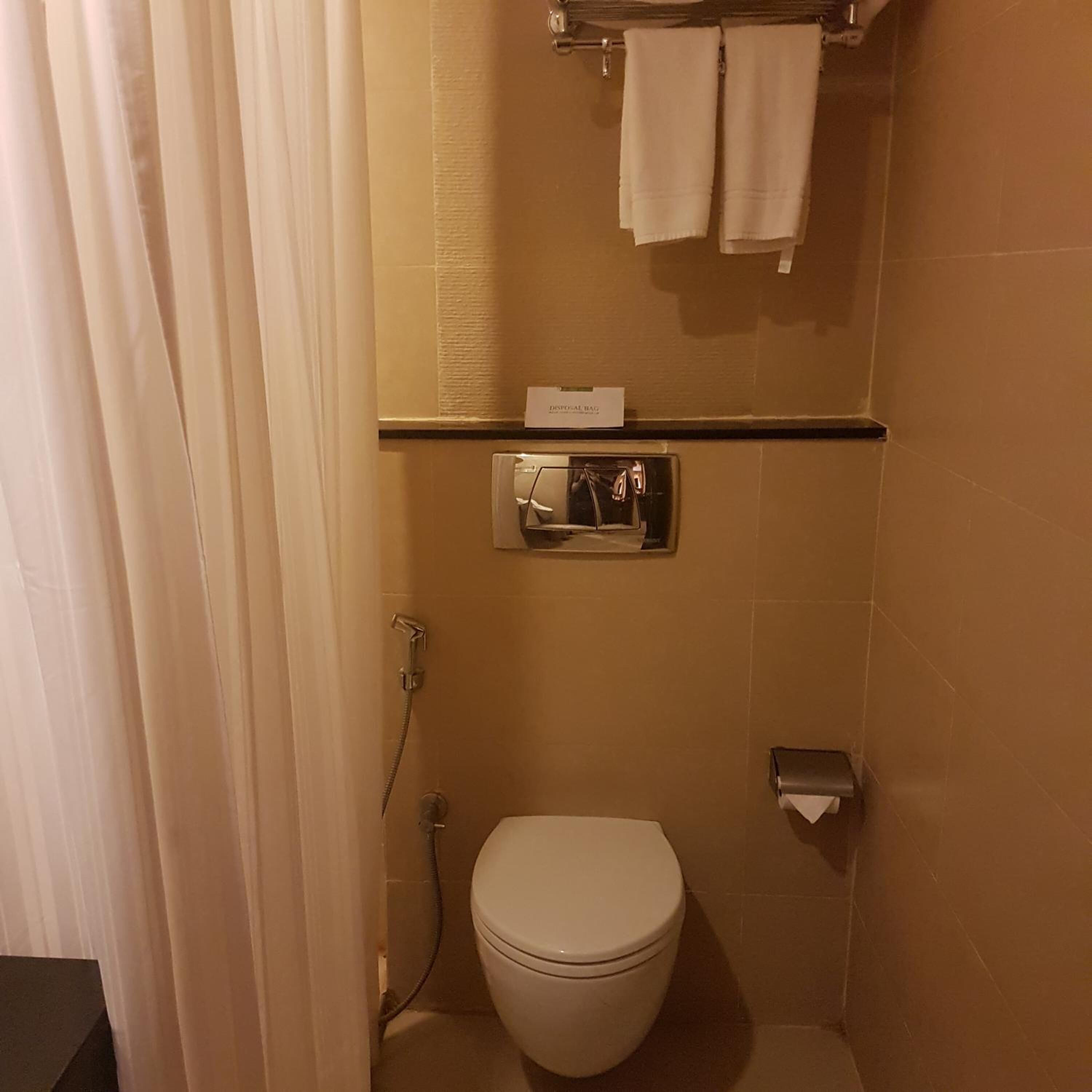 A small, compact bathroom with a toilet, a towel rack, and a disposal bag.