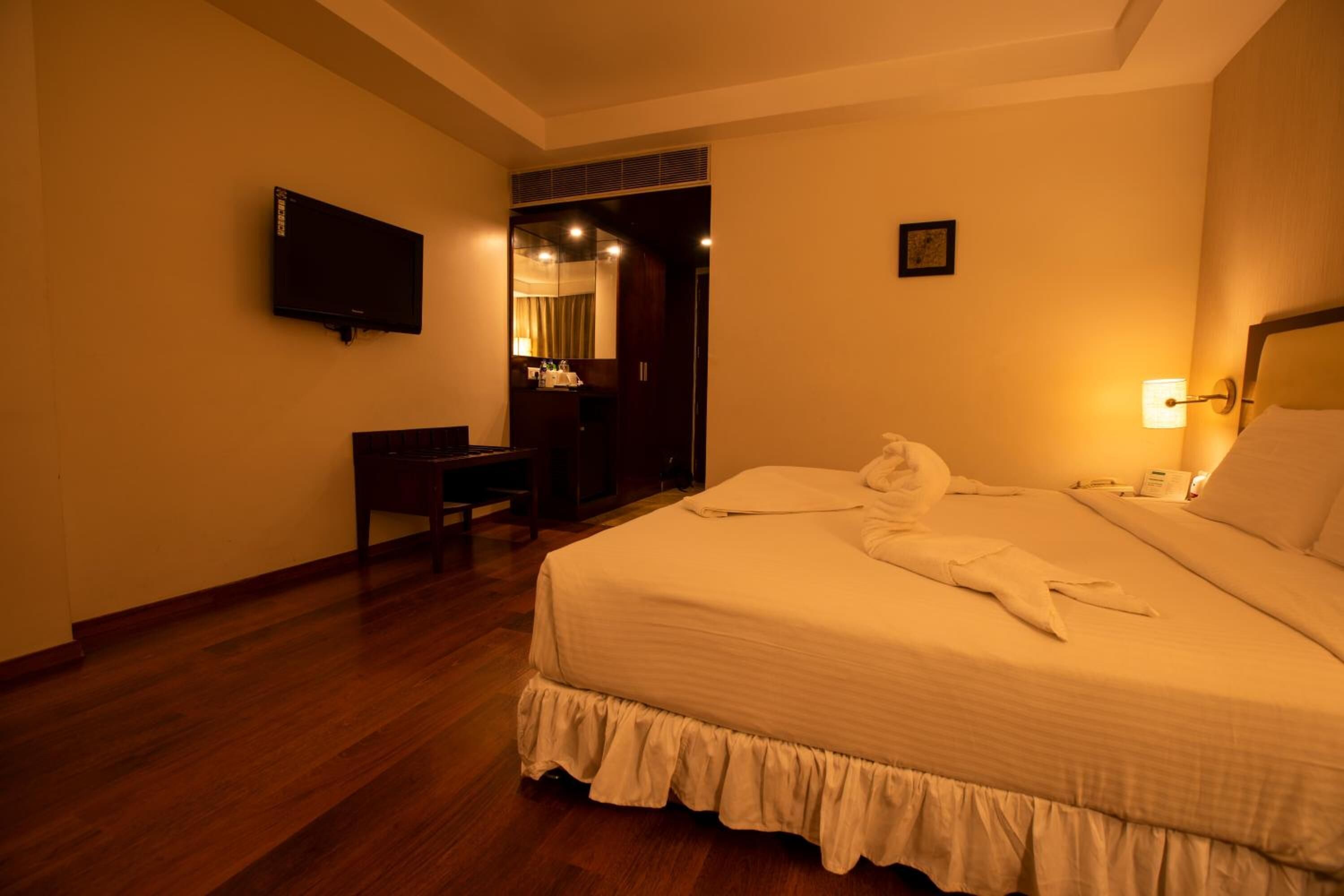 Una habitación de hotel con una cama grande, un escritorio, un televisor y un espejo.