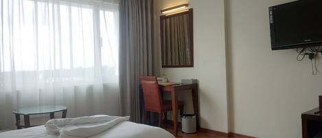 A hotel room with a bed, a desk, a chair, a television, and a window with curtains.