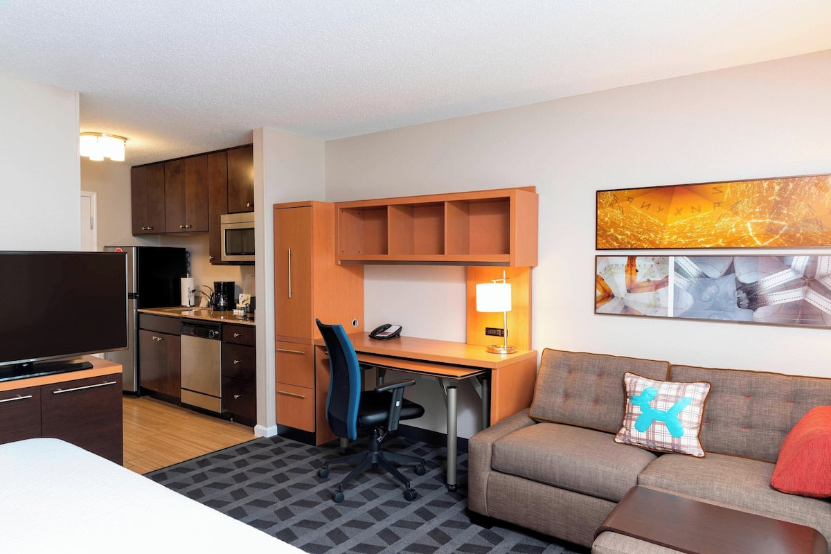 A hotel room with a kitchenette, a sofa, a desk, and a TV.