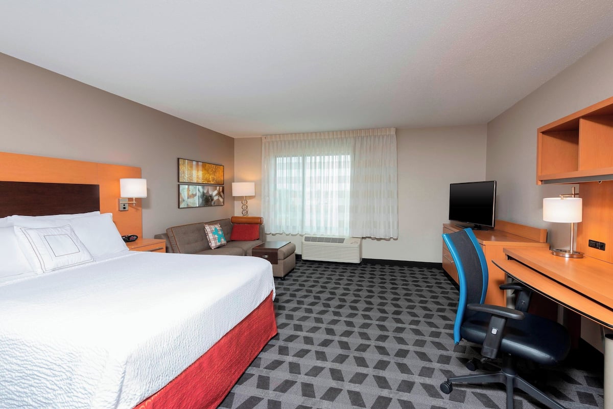 A hotel room with a large bed, a desk, a chair, a television, and a window with curtains.
