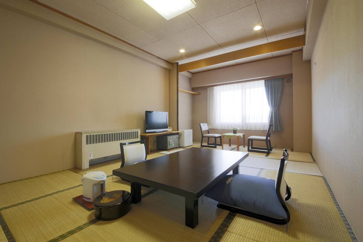 A room with tatami flooring, a television, a dining table, and a sofa.