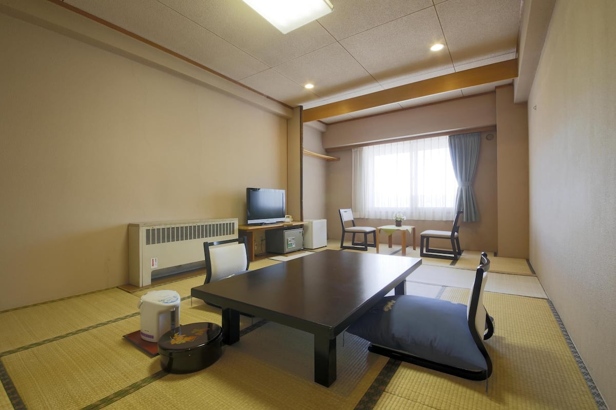 A room with tatami flooring, a television, a dining table, and a sofa.