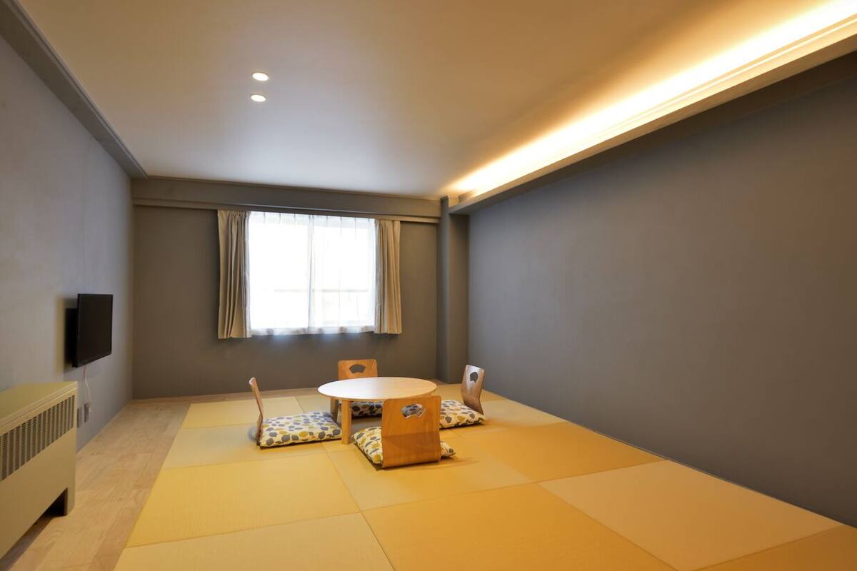 A room with tatami mats, a round table, and chairs with cushions.