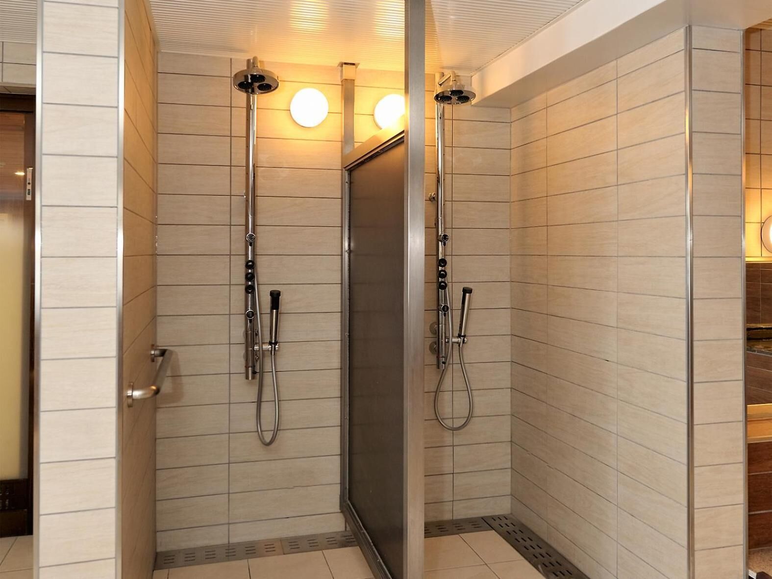 Un espace douche moderne doté de deux pommes de douche, d’une porte en verre et de murs carrelés.