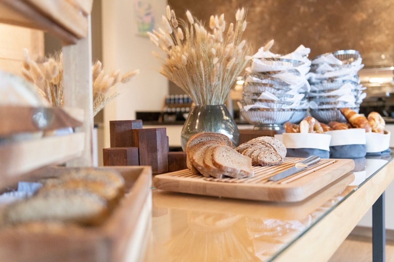Mostrador de panadería con hogazas de pan, tabla de cortar y un florero con flores secas.