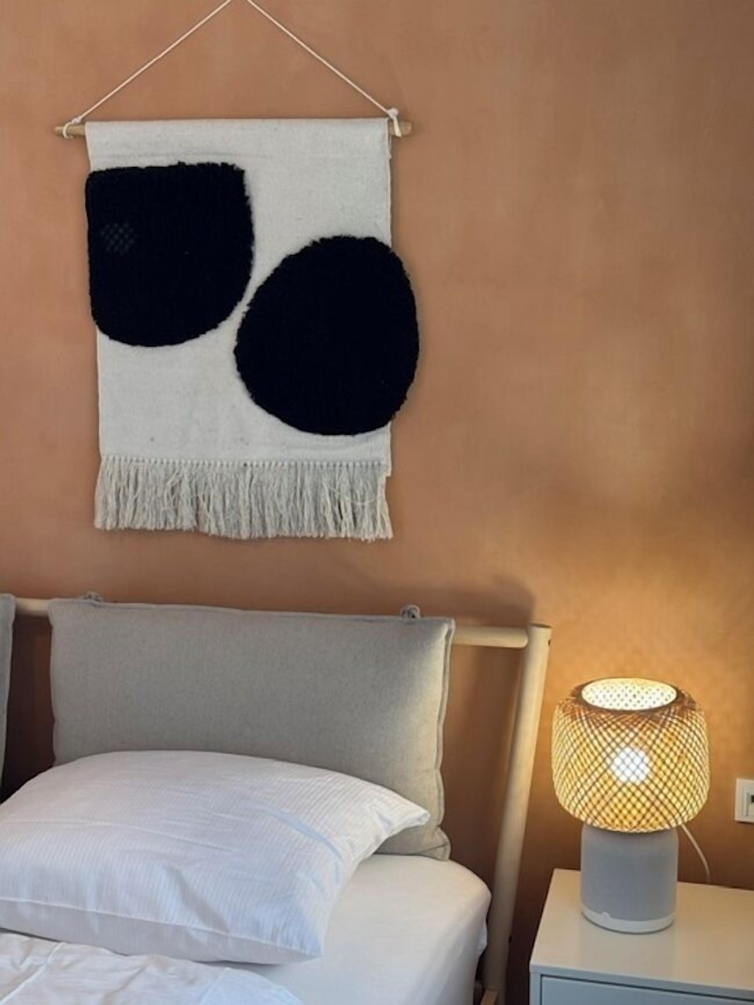 Quarto com cama, abajur e um objeto pendurado na parede.