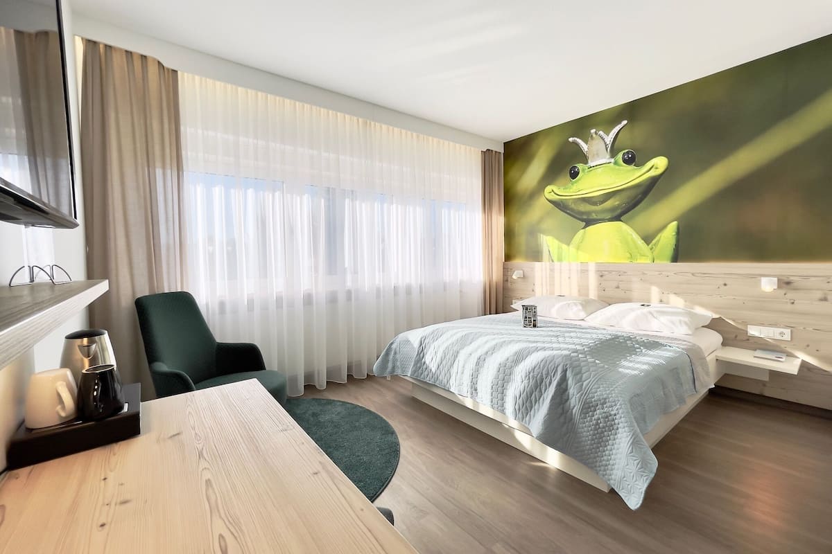 A hotel room with a bed, a desk, a chair, a TV, and a large wall mural.
