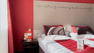 A neatly arranged bedroom with a red carpet, a bedside table with a lamp, and a bed with a red and white bedspread.