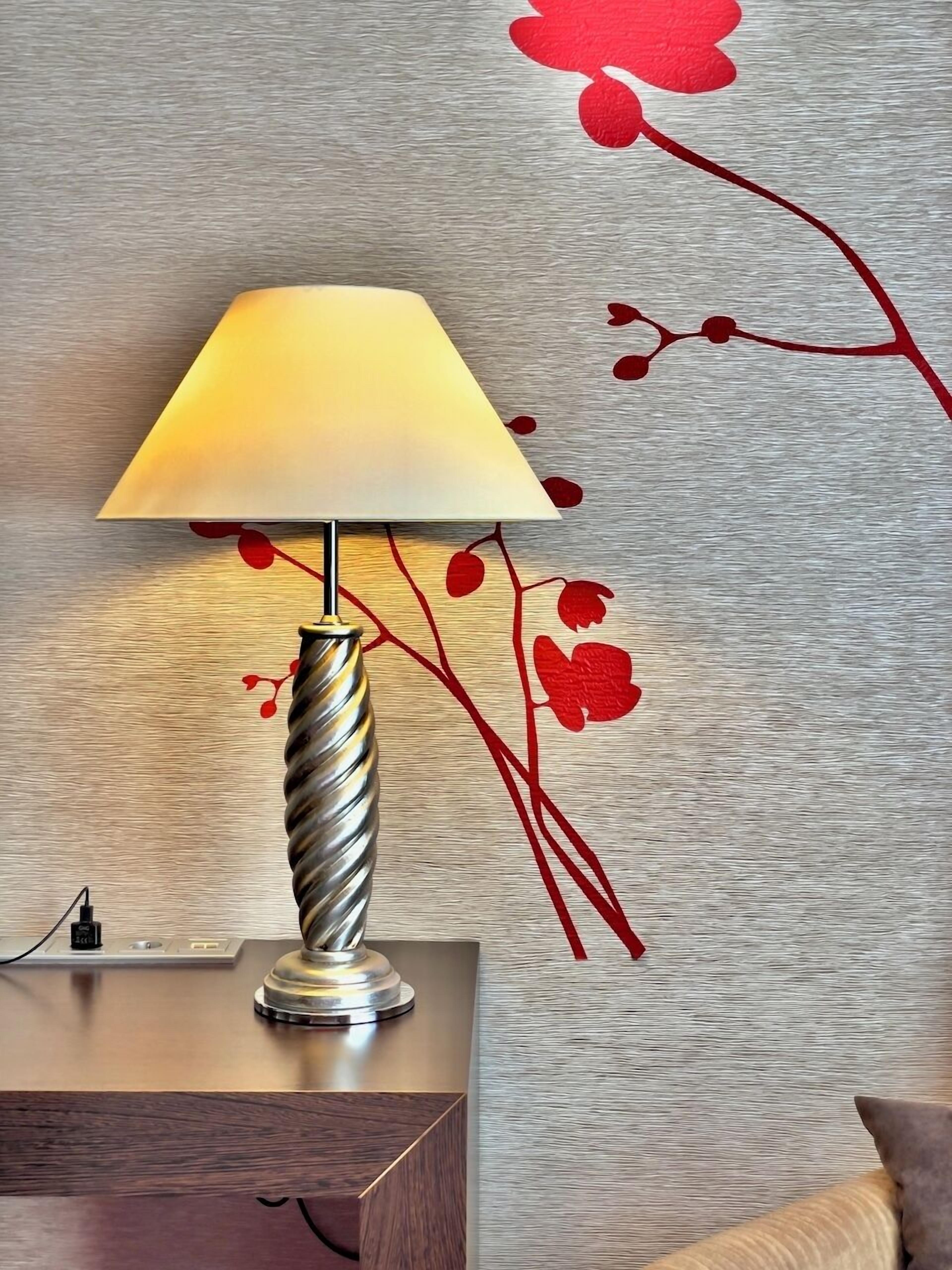 A lamp with a metallic base and a white lampshade on a wooden surface.