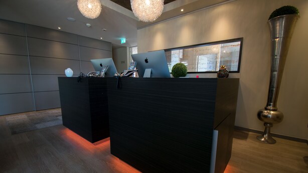 A reception desk with two laptops, a framed wall with handwritten notes, and a tall metallic vase. - ART-Hotel Braun (Kirchheimbolanden)