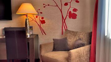 A hotel room with a sofa, a desk, a lamp, a TV, and a red carpet.