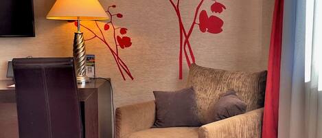 A hotel room with a sofa, a desk, a lamp, a TV, and a red carpet.