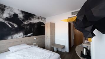 Een moderne hotelkamer met een groot bed, een houten hoofdbord, een kunstwerk aan de muur, een bureau en een koffieapparaat.