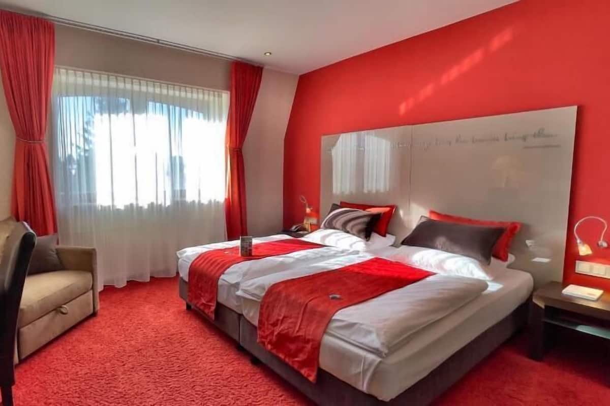 A hotel room with a large bed, a desk, a chair, and a window with curtains.