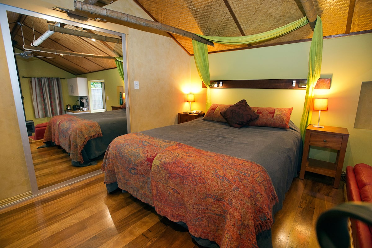 Une chambre à coucher avec un grand lit, deux tables de chevet avec des lampes, un miroir et un fauteuil rouge.