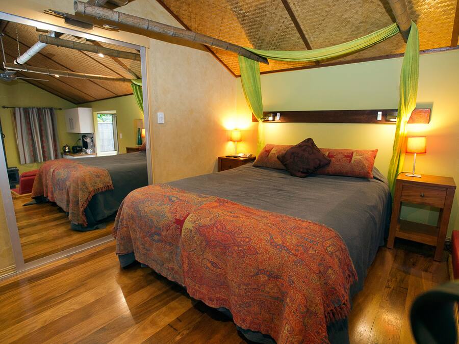 A bedroom with a large bed, two bedside tables with lamps, a mirror, and a red chair.